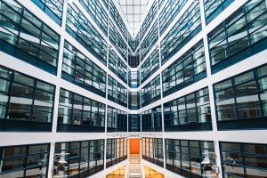 Modern Office Building Interior With Symmetrical Glass Windows and Bright Architecture Featuring a Staircase at the Core, Creating a Futuristic Perspective in a Contemporary Urban Work Environment A symmetrical view of a modern office building interior featuring large glass windows, sleek architecture, and a central staircase, reflecting a bright, contemporary workplace atmosphere.